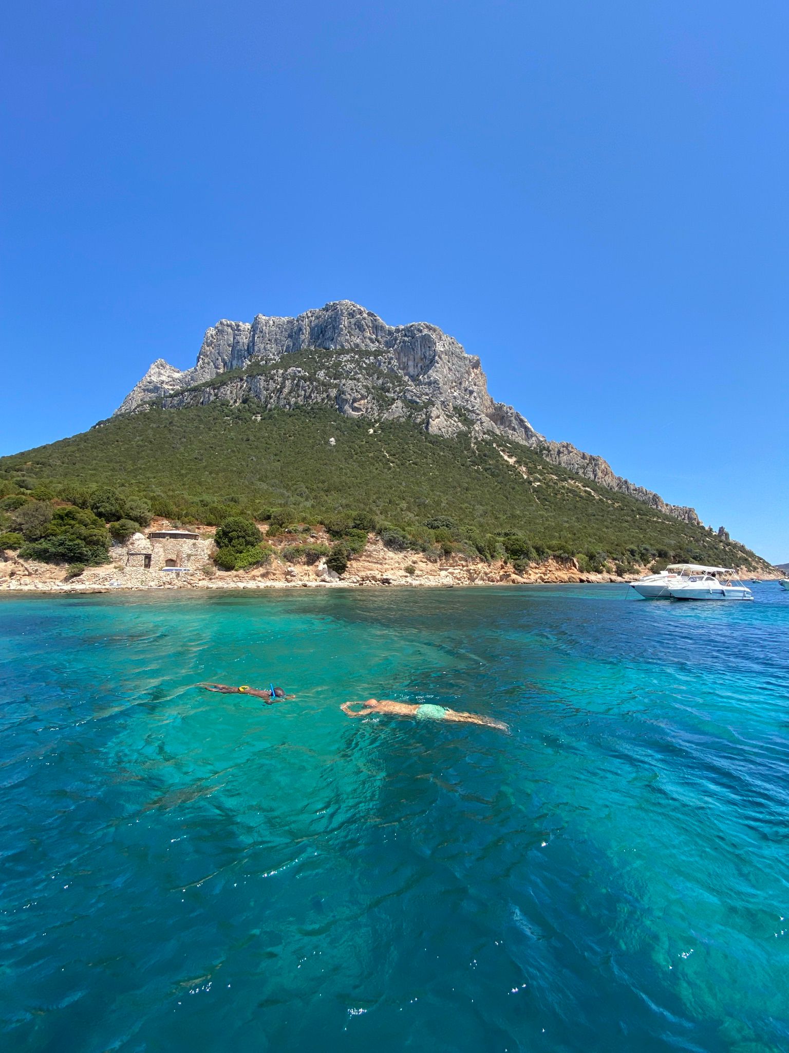 Tavolara Island rising above turquoise water with swimmers and a boat offshore