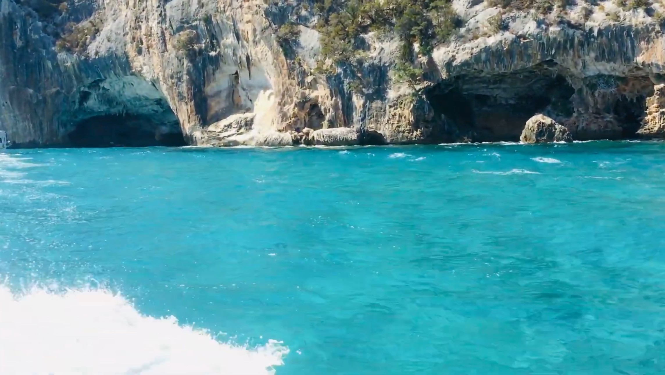 Sea-cave openings in limestone cliffs above turquoise water along the Gulf of Orosei